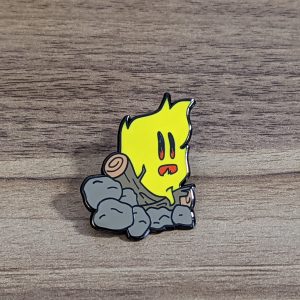 Campfire Hard enamel pin on a wooden background. Yellow fire, burning on wood logs and rocks.