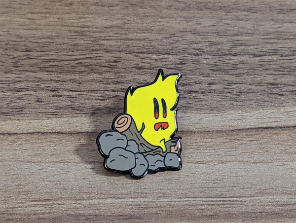 Campfire Hard enamel pin on a wooden background. Yellow fire, burning on wood logs and rocks.