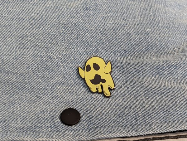 Ghost pin with arms high and drooling. Beige colour. Fitted to denim.