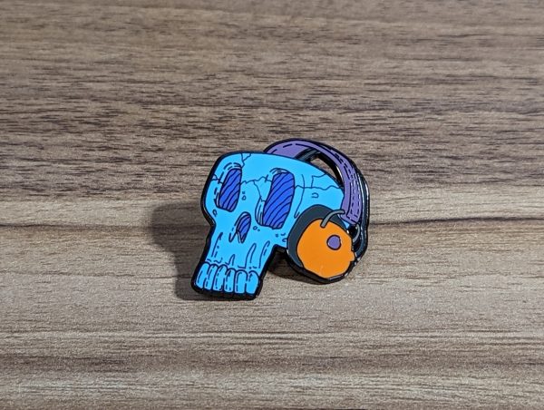 Blue Skull wearing headphones hard enamel pin. The headphones are orange with a purple strap.