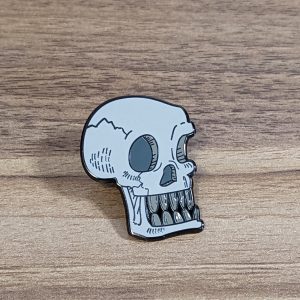 This skull pin has a bone to pick! The skull is grey with their teeth bared!