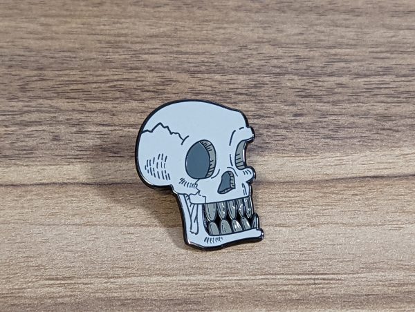 This skull pin has a bone to pick! The skull is grey with their teeth bared!