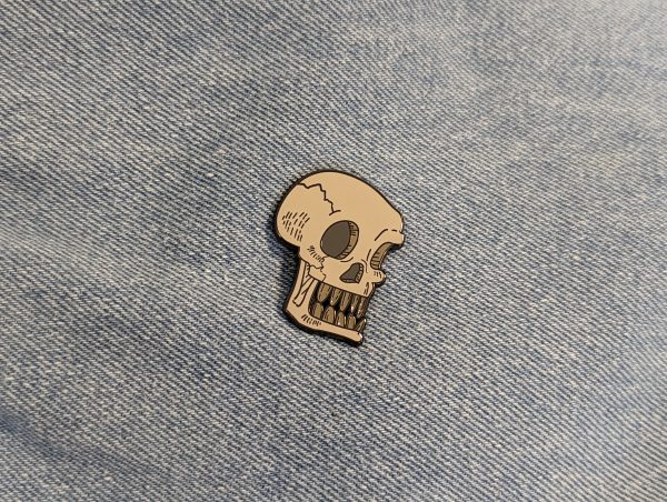 This skull pin has a bone to pick! The skull is grey with their teeth bared! It looks so punk on denim!