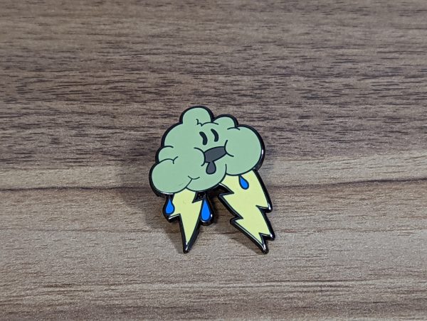 The storm cloud hard enamel pin is grey with yellow lightning bolts and blue rain drops. The pin has a drooling face!